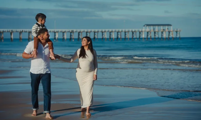 Family walking a beach by a pier